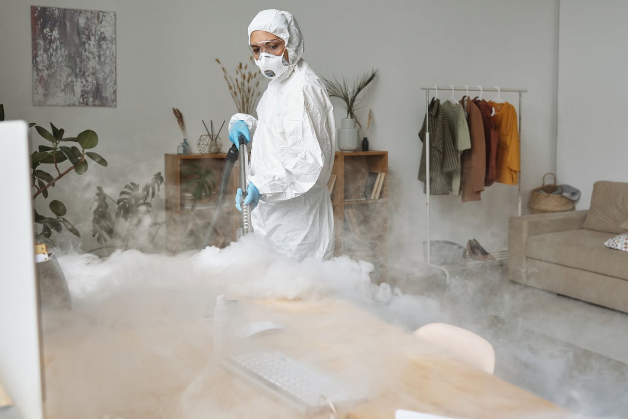 A professional in PPE disinfecting an indoor space using fumigation for safety.