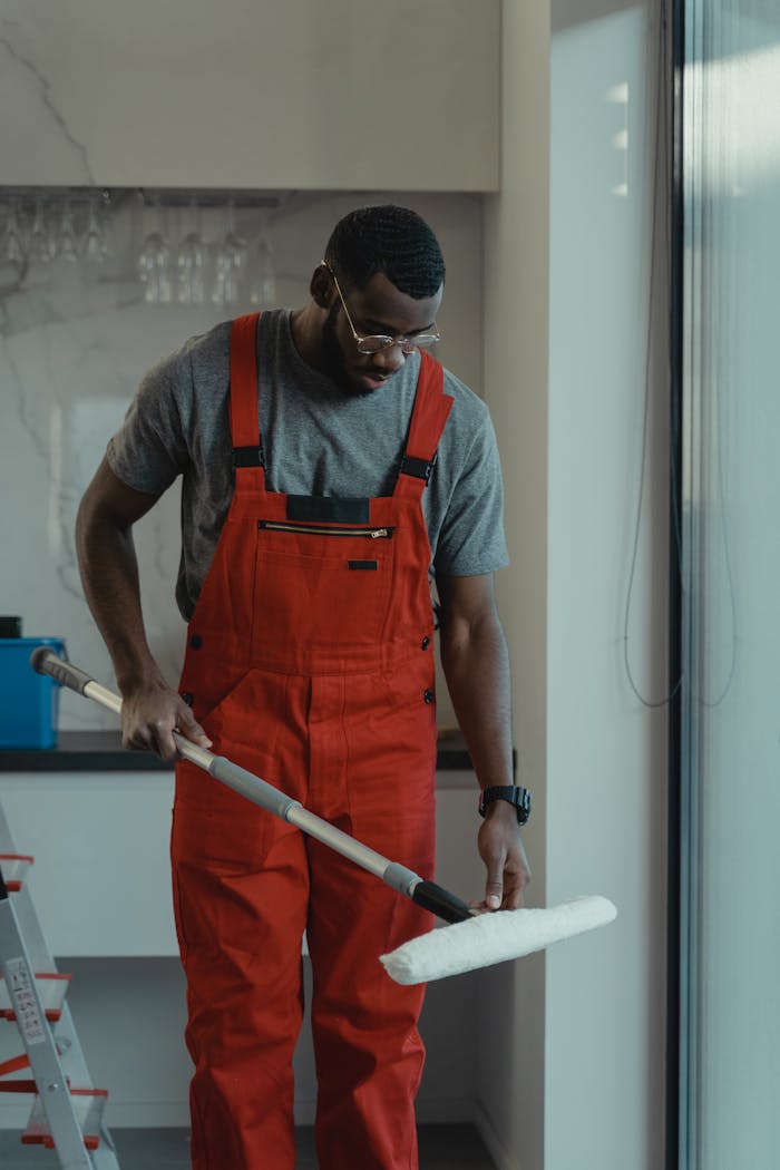 Man wearing red overalls using a mop indoors, depicting cleanliness and manual work.